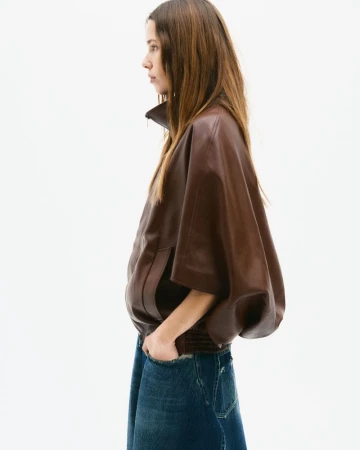 Model in brown leather jacket and blue denim jeans standing against white seamless background