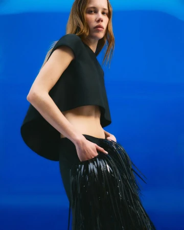 Model in a black top and fringed skirt against a vivid blue background for CR Fashion Book photographed by Xavier Casanueva