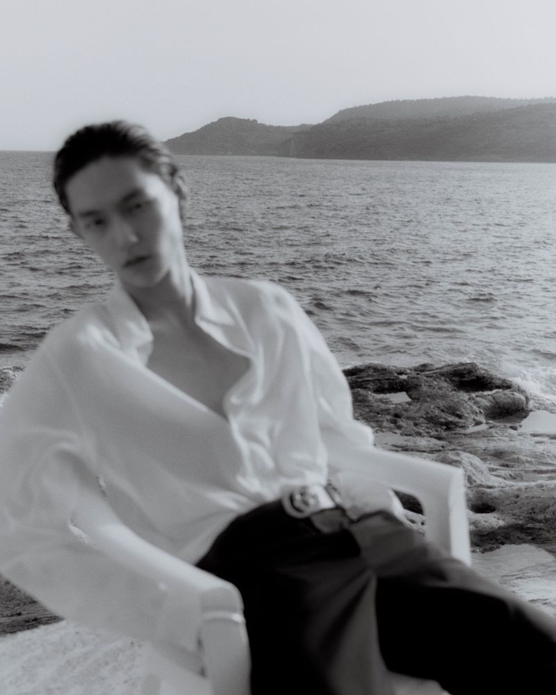 Monochrome fashion portrait of a model in a white shirt seated in a plastic chair by the ocean