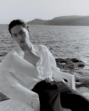 Monochrome fashion portrait of a model in a white shirt seated in a plastic chair by the ocean