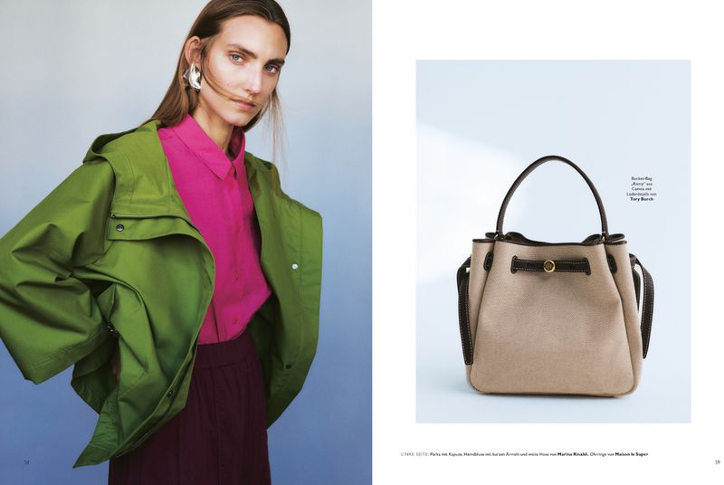 Fashion editorial shot of a young woman in a green jacket and pink shirt, and a beige bucket bag with brown trim on a white background.