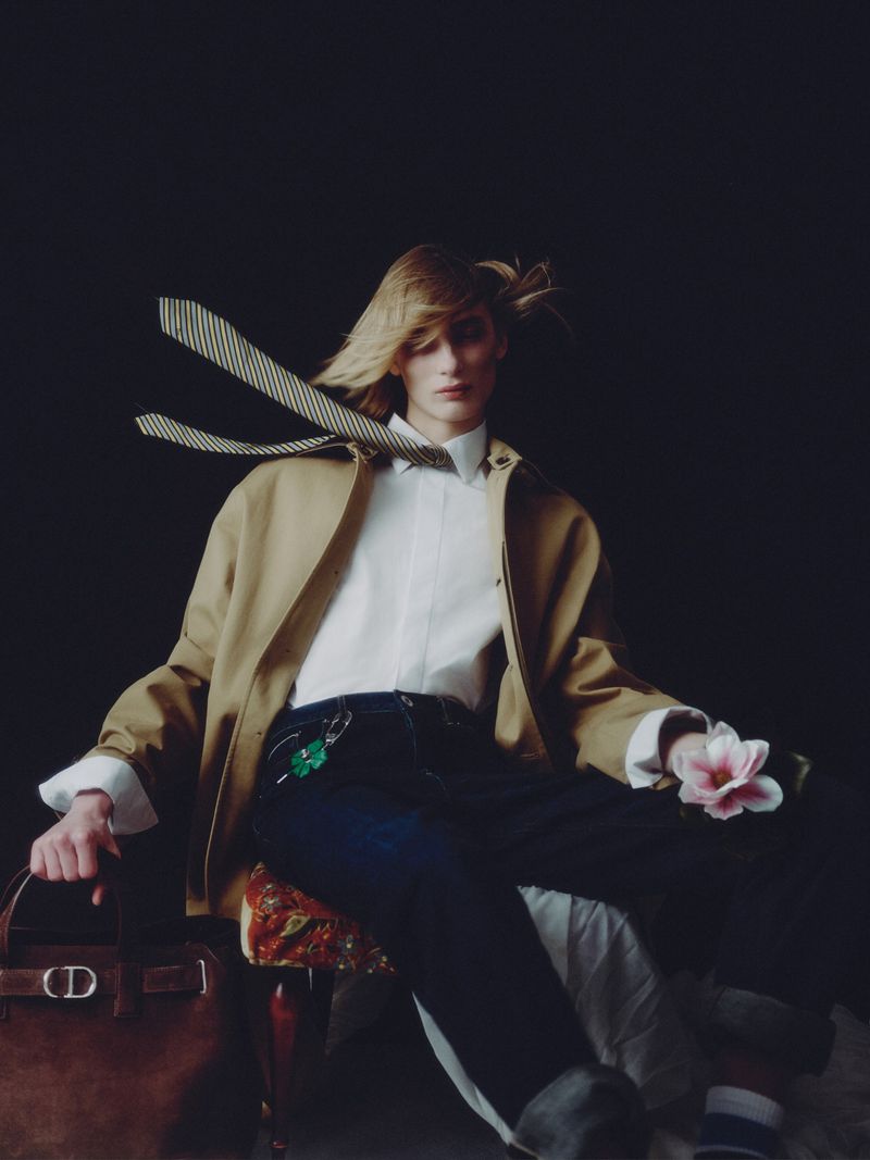 Model with blowing hair wearing a tan jacket and white shirt holding a flower for Greatest Magazine DIOR project.