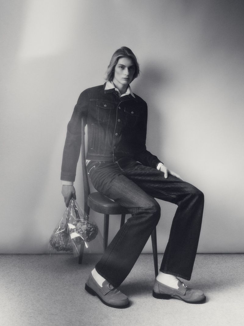 Model Nand Quivreux seated on a chair holding wrapped flowers in a studio portrait for Greatest Magazine DIOR project
