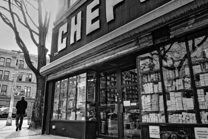 Black and white photograph of a man walking past the storefront of CHEF Restaurant Supply store on a city street with bare trees.