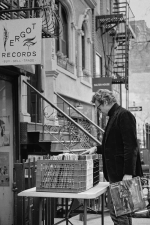 Black and white image of a man browsing records outside a shop with a sign that reads 'Ergot Records Buy Sell Trade'.