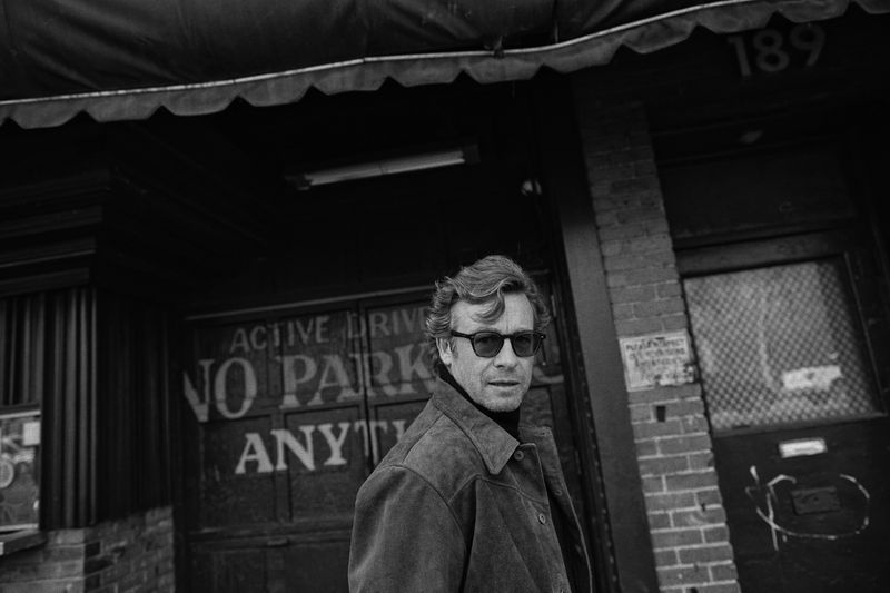Black and white portrait of a man with sunglasses in front of an urban building with textured walls and awning.