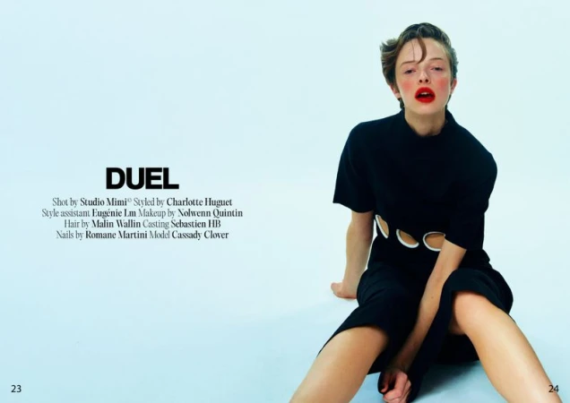 Model wearing a black cut-out dress seated against a light blue seamless background for Duel Magazine