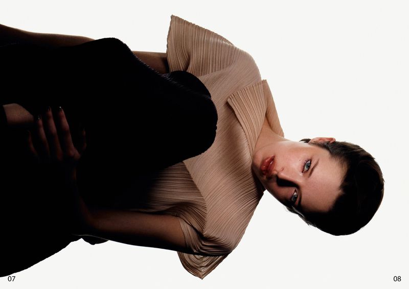 Model wearing a pleated beige top and dark skirt against a plain white background for Duel Magazine