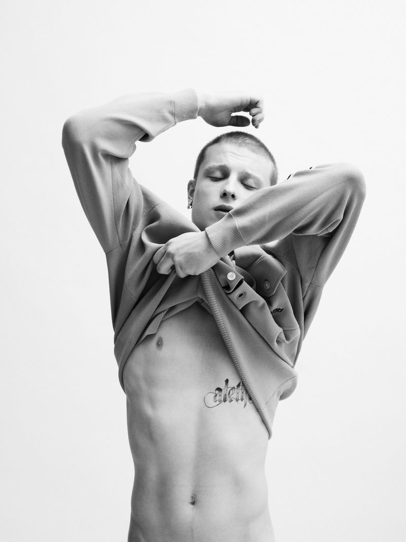 Portrait of actor Francesco di Tullio lifting his sweatshirt against a plain white studio background