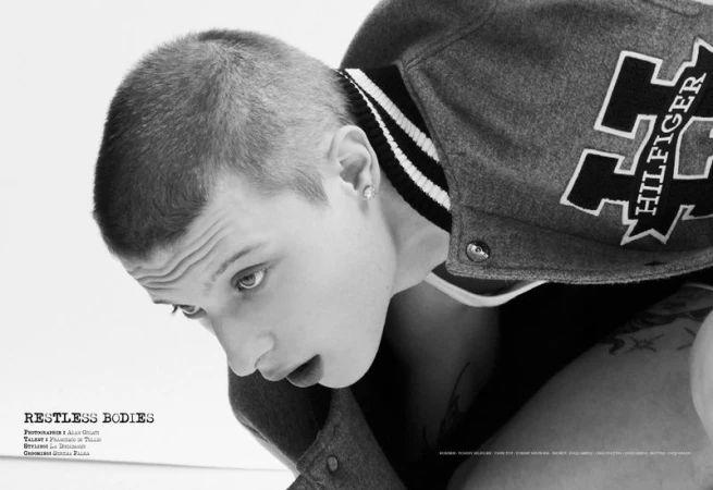 Close-up black and white portrait of actor Francesco di Tullio wearing a varsity jacket and earring against a white background.
