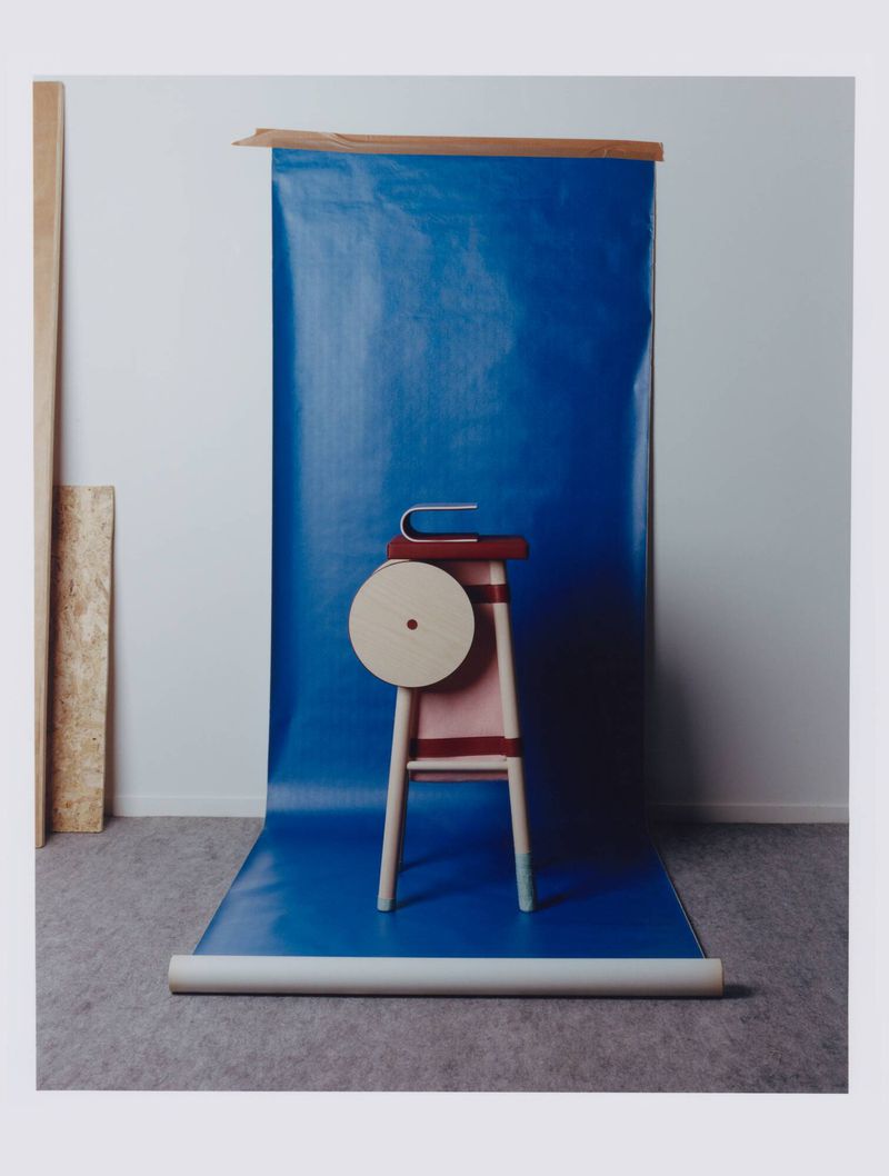 Wooden stool with a round circular top object and metallic element set against a vibrant blue backdrop roll in a studio.