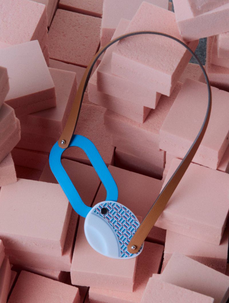 Blue and tan leather necklace resting on a textured arrangement of pink rectangular blocks.