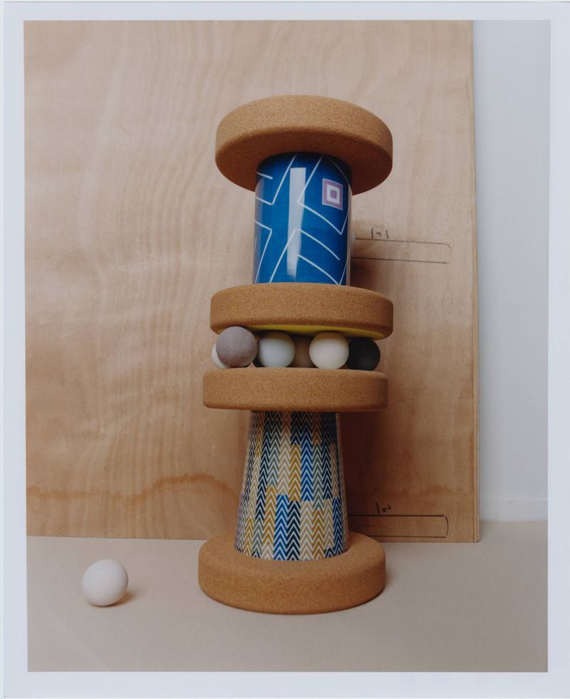 Sculptural tower installation of stacked cork discs, blue patterned cylinders, and small spheres on a light surface.