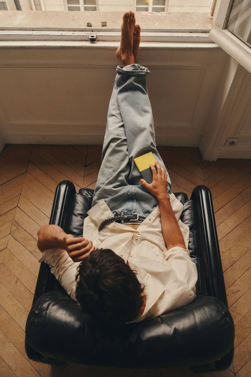 Overhead shot of a man relaxing in a black leather armchair wearing light wash jeans and a white shirt with feet resting on a windowsill