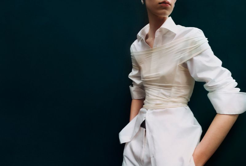 Model wearing a white shirt styled with layered wrapping against a dark background for an editorial feature.