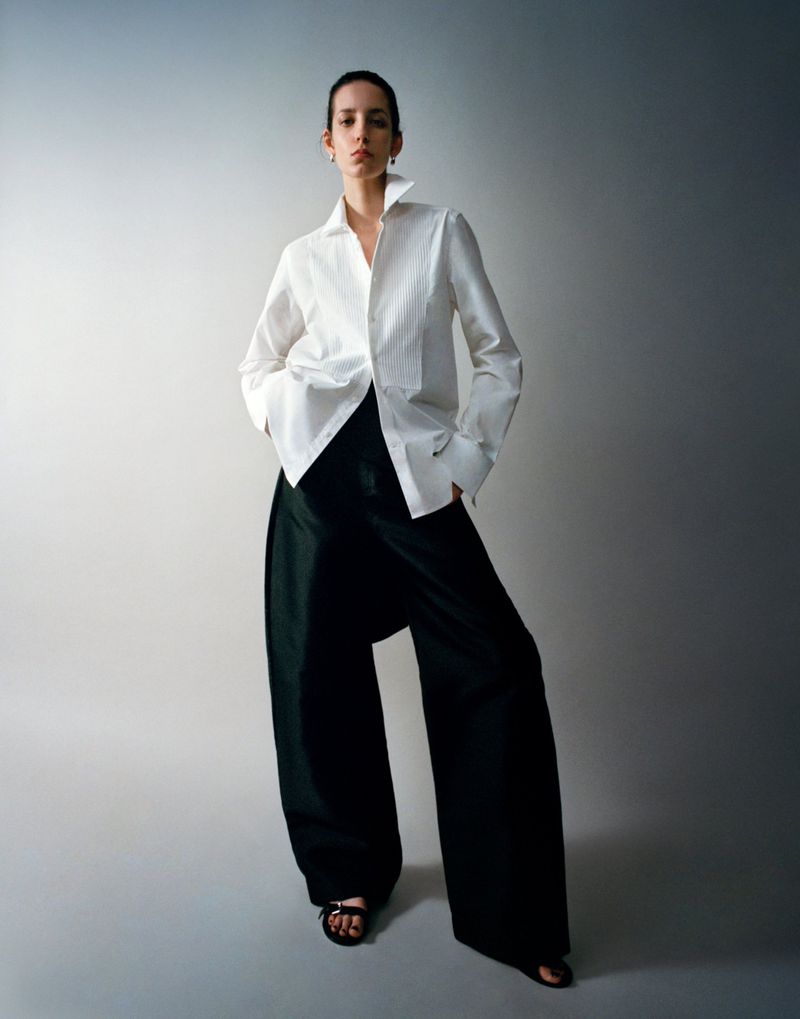 Model wearing a white shirt and black trousers against a neutral grey studio backdrop captured by photographer Rodrigo Carmuega.
