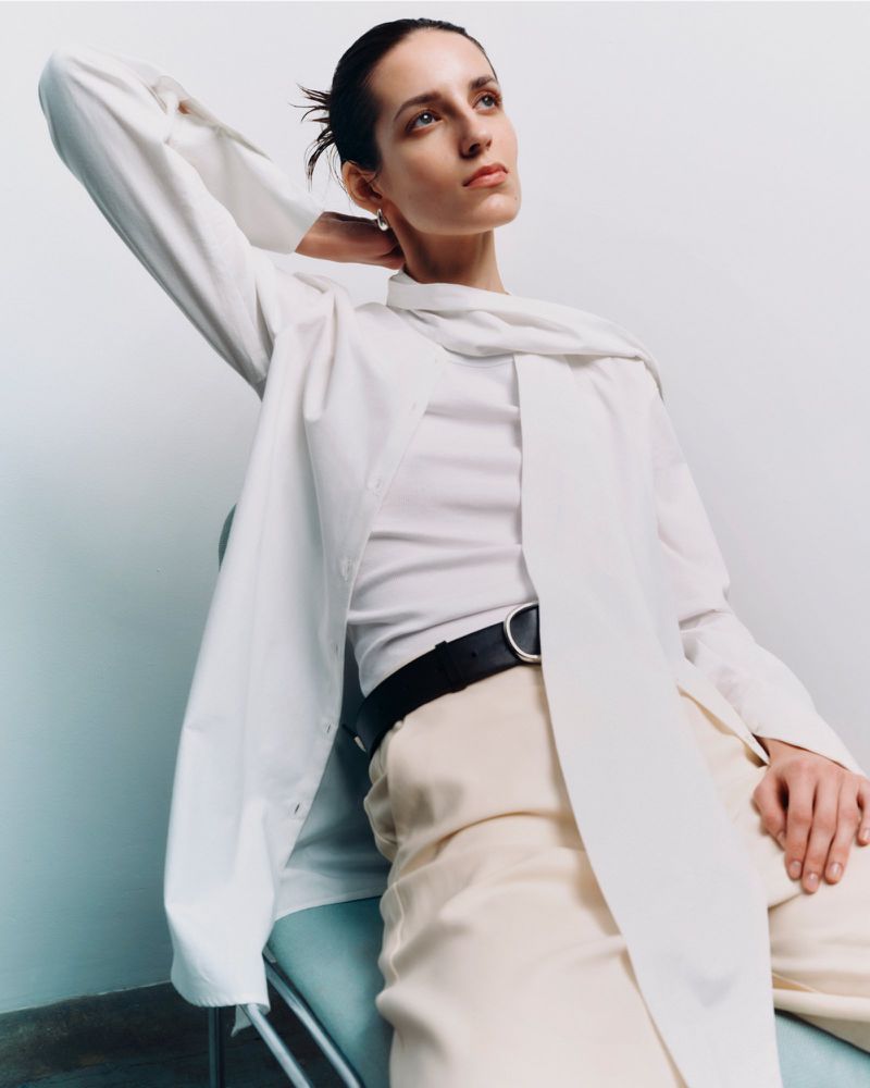 Model wearing a white shirt and trousers seated against a light background for an editorial project by Financial Times HTSI Magazine.