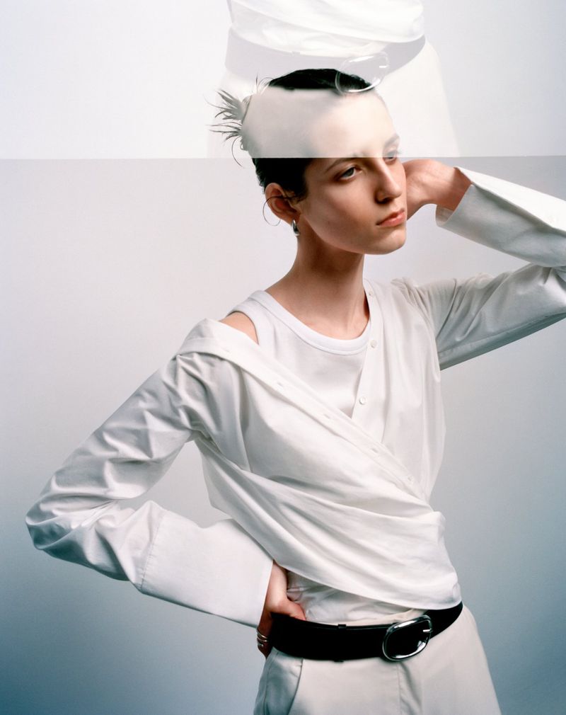 Model wearing a layered white shirt and black belt against a white seamless background with a double exposure effect.