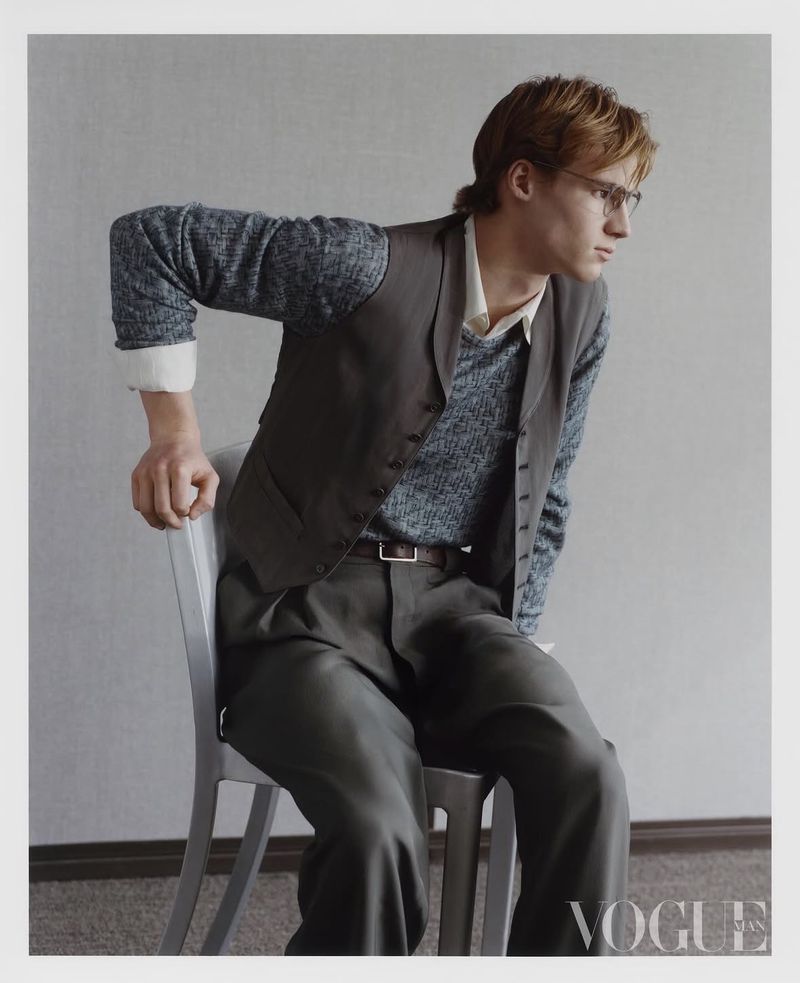 Model in grey vest and trousers seated on a chair against a plain grey background for Vogue China Men editorial