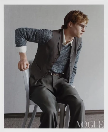 Model in grey vest and trousers seated on a chair against a plain grey background for Vogue China Men editorial