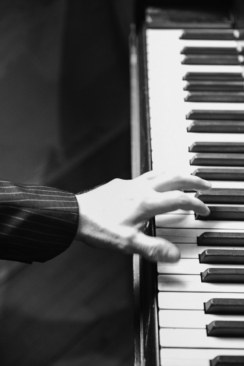 Monochrome image of a person's hand playing a piano, focusing on the keys and the hand's position during the musical performance.
