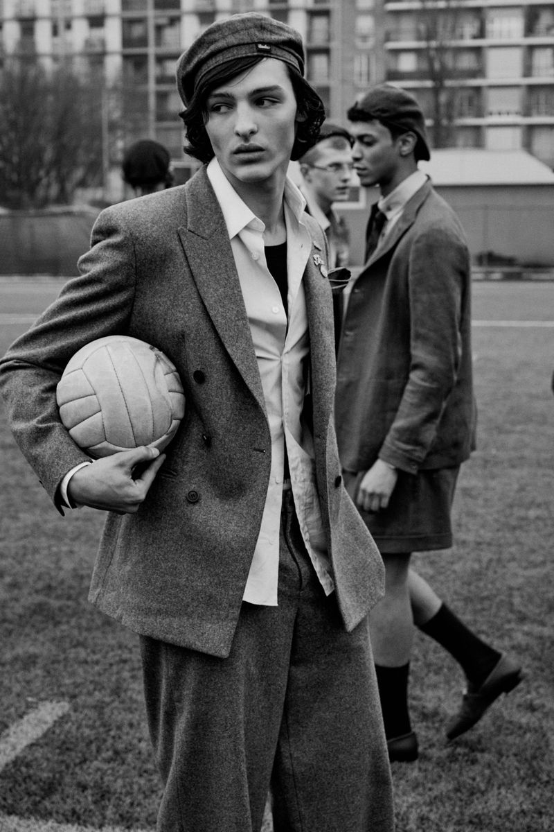 Monochrome fashion editorial image featuring a young male model in a tweed suit holding a vintage football outdoors.