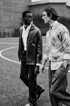 Two male models walking together on an outdoor sports field wearing contemporary menswear fashion apparel.