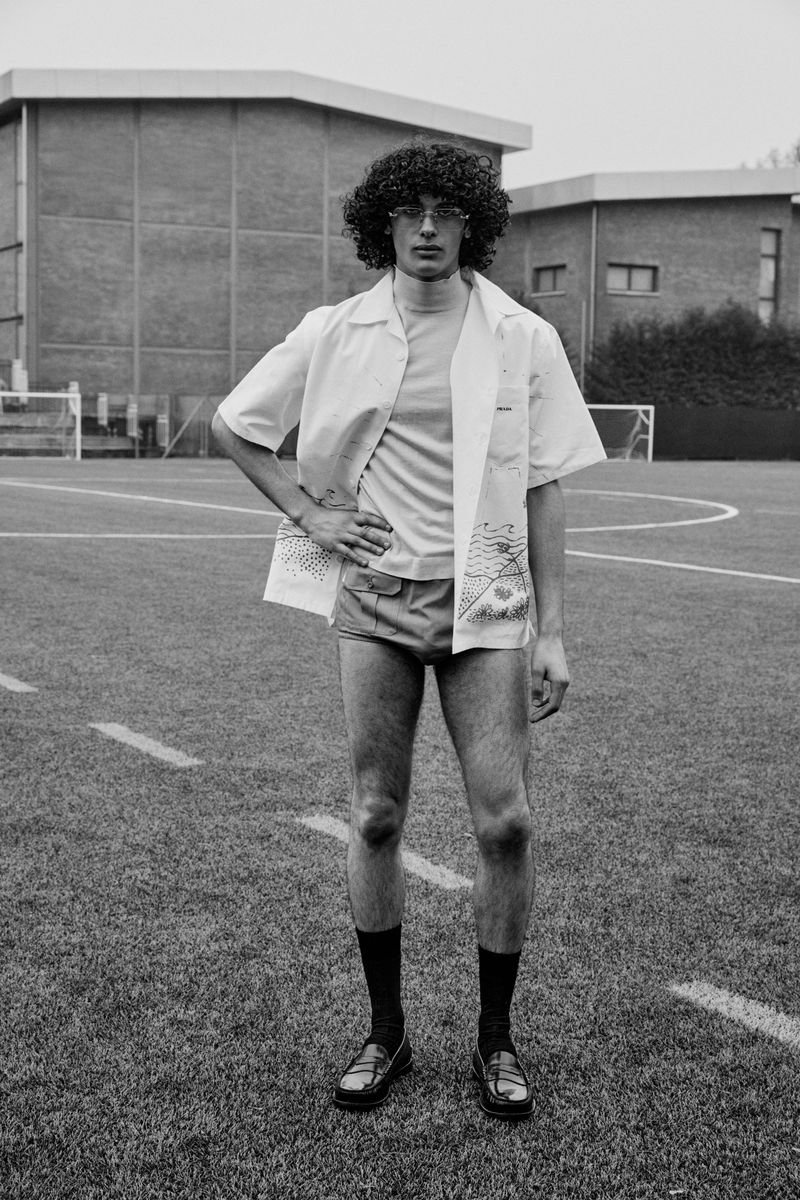 Model with curly hair and glasses wearing a white button-down shirt on a soccer field for L'Officiel Hommes Italia.