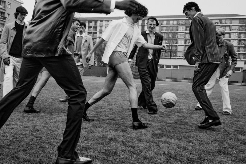 Group of men playing soccer on a grassy field in front of apartment buildings for L'Officiel Hommes Italia editorial