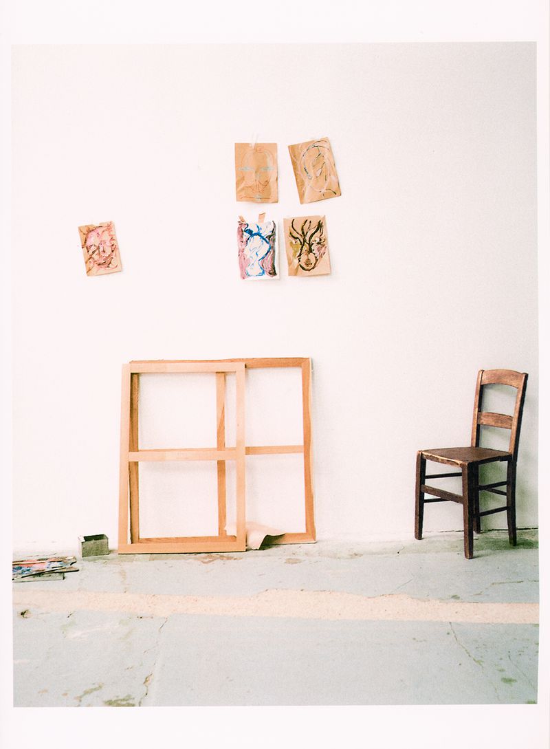 An artist studio interior featuring empty wooden frames, a small wooden chair, and pinned sketches against a plain white wall