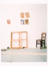 An artist studio interior featuring empty wooden frames, a small wooden chair, and pinned sketches against a plain white wall