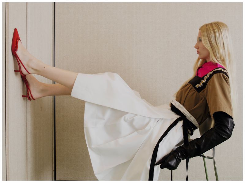Blonde model in a white skirt with red heels pressed against the wall for Elle Greece Quiet Bloom