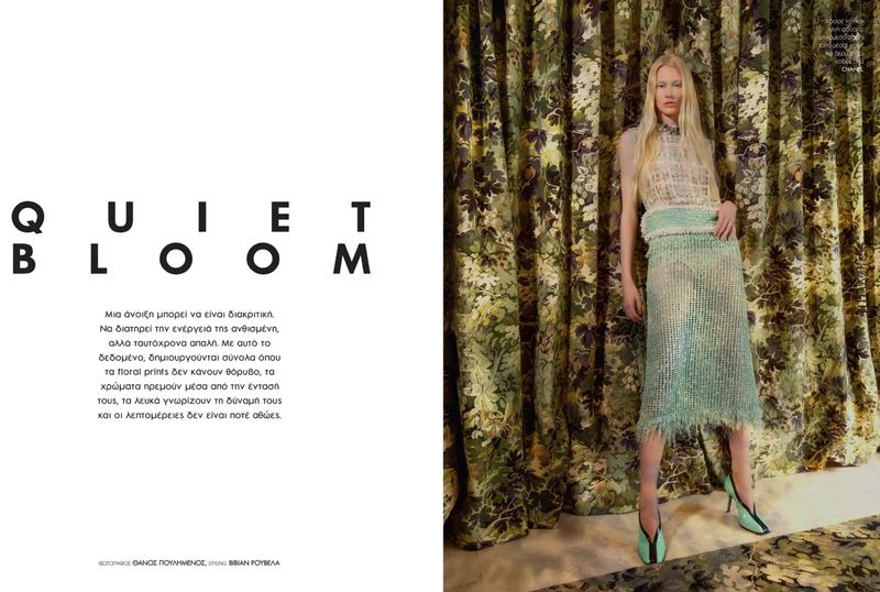Blonde female model wearing green textured skirt and top standing in front of patterned floral drapes for Elle Greece.