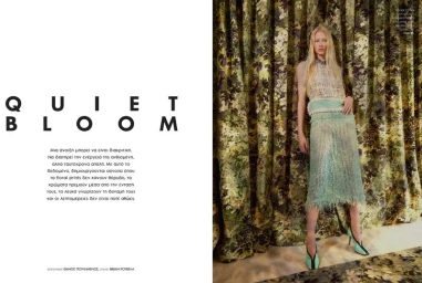 Blonde female model wearing green textured skirt and top standing in front of patterned floral drapes for Elle Greece.