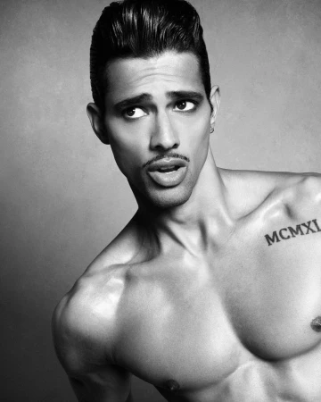 Portrait of model Jonas Barros with styled hair and a shoulder tattoo against a plain grey studio backdrop