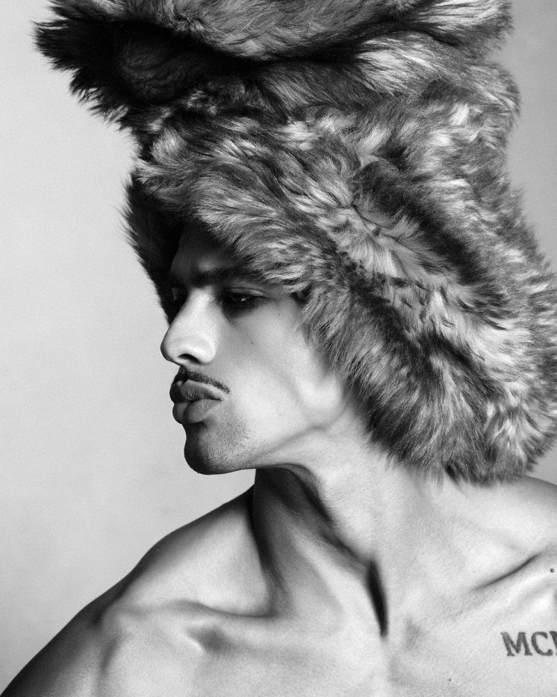 Model Jonas Barros wearing a large furry hat and profile view in a black and white fashion portrait for Double Vision.
