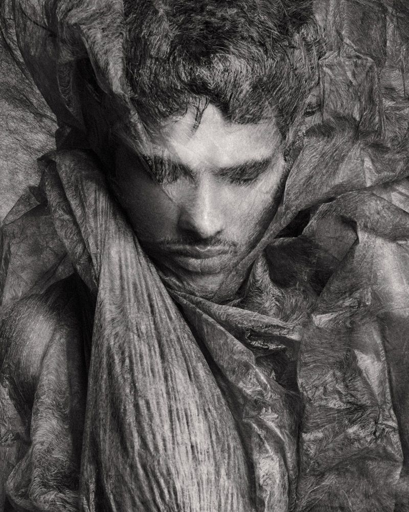 Close-up portrait of male model Jonas Barros wrapped in textured translucent material in monochrome
