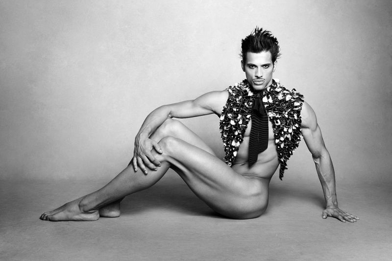 Model Jonas Barros seated on a grey seamless backdrop wearing a textured floral vest and dark tie.