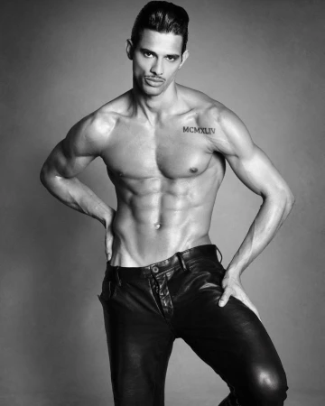 Shirtless male model Jonas Barros wearing black leather trousers posing against a grey studio backdrop