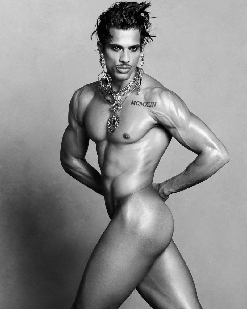 Model Jonas Barros posing shirtless wearing ornate pendant necklaces in a monochrome studio portrait