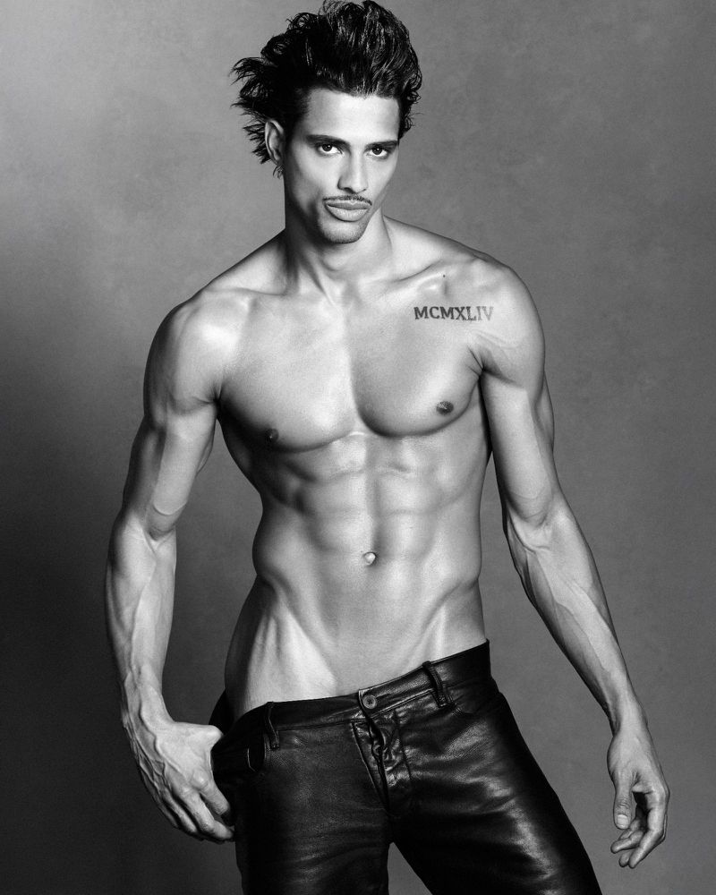 Shirtless male model Jonas Barros wearing dark trousers against a textured grey studio background