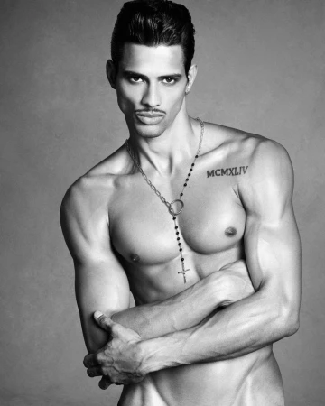 Portrait of Jonas Barros wearing a pendant necklace against a plain grey backdrop in a black and white editorial photograph.