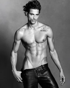 Shirtless male model Jonas Barros wearing dark trousers against a textured grey studio background