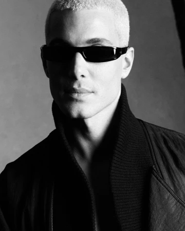 Fai Khadra wearing dark sunglasses and a dark high-collar jacket in a monochrome portrait shot by Luigi and Iango for Double Vision.