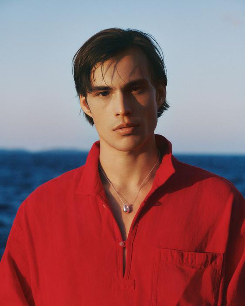 Portrait of a man wearing a bright red collared shirt with a silver necklace against an out of focus blue ocean background.