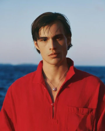 Portrait of a man wearing a bright red collared shirt with a silver necklace against an out of focus blue ocean background.