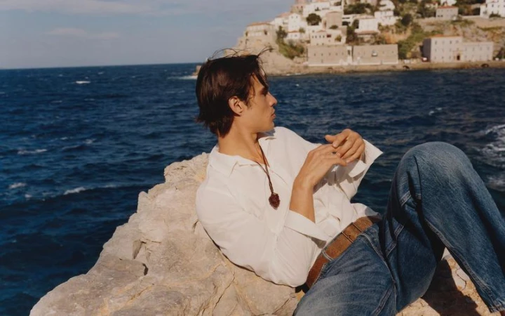 Model Louis Baines reclining on coastal rock formations overlooking deep blue ocean water for Zara Man campaign.