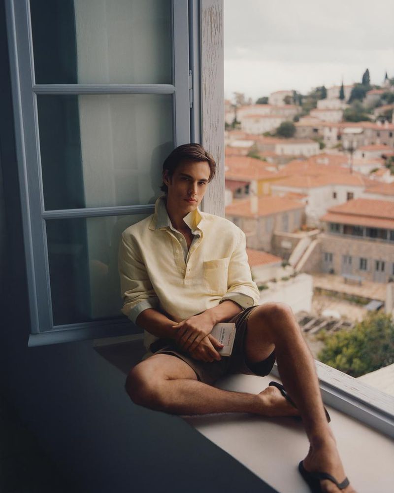 Model Louis Baines seated on a windowsill wearing a yellow polo shirt for Zara Man Spring 2026, photographed by Ronan Gallagher.