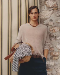 Male model Louis Baines wearing a beige knit sweater and dark trousers holding a straw bag for Zara Man Spring 2026