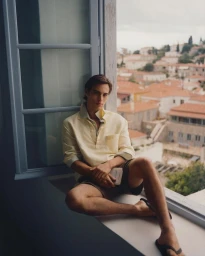 Model Louis Baines seated on a windowsill wearing a yellow polo shirt for Zara Man Spring 2026, photographed by Ronan Gallagher.